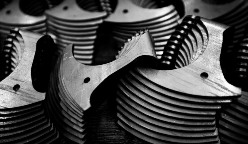 The black-and-white image shows a close-up of stacked metal components with fine milling structures and drill holes. The high-precision edges and symmetrical shapes reflect the exacting manufacturing standards of weba Germany’s prototyping. This image highlights the quality and precision required for complex components in the automotive industry.