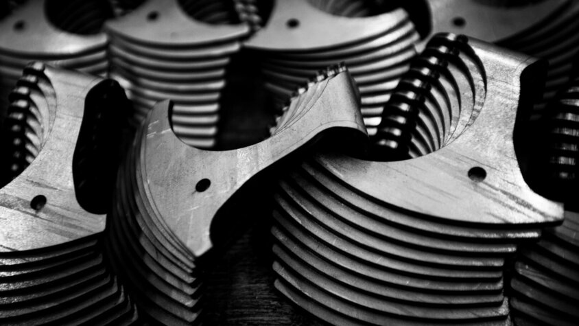 Das Schwarz-Weiß-Bild zeigt eine Nahaufnahme gestapelter Metallbauteile mit feinen Frässtrukturen und Bohrungen. Die hochpräzisen Kanten und symmetrischen Formen stehen für die exakte Fertigung im Prototypenbau von weba Deutschland. Dieses Bild unterstreicht die Qualität und Präzision, die für komplexe Bauteile in der Automobilindustrie erforderlich sind.