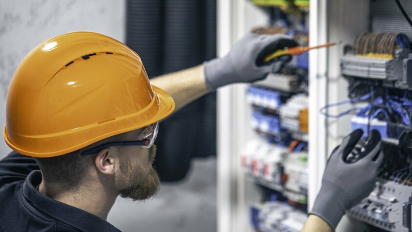 Elektromechaniker mit Schutzhelm prüft elektrische Steuerung und Verkabelung in einem Schaltschrank