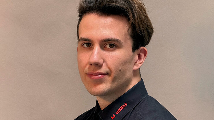 Portrait photo of Michal Urbuś, IT technician at weba Werkzeugbau, wearing a black shirt with a red weba logo, in front of a neutral background.