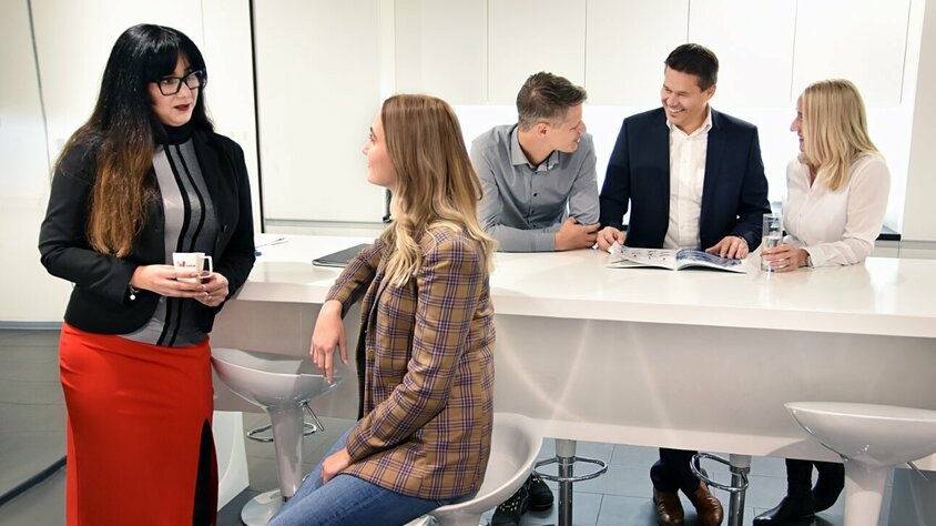 Mitarbeiterinnen und Mitarbeiter von weba Werkzeugbau entspannen sich während der Pause und führen angeregte Gespräche in der Kaffeeküche des Unternehmens.