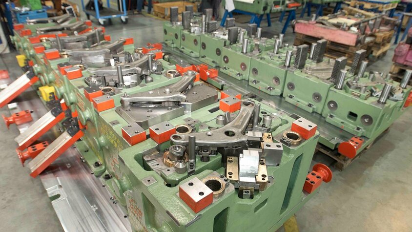 Transferwerkzeug für einen Querlenkerarm in der Automobilproduktion; komplexe Werkzeugaufspannung mit mehreren Formnestern und mechanischen Einheiten in der Werkhalle von weba Werkzeugbau.