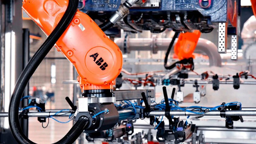 Series Production at weba Werkzeugbau An industrial robotic arm in tool manufacturing working on a complex production line. The orange ABB robotic arm is equipped with various gripping and sensor tools and is used in series production and forming technology. In the background, additional mechanical components and wiring emphasize the state-of-the-art automation and precision in manufacturing technology.