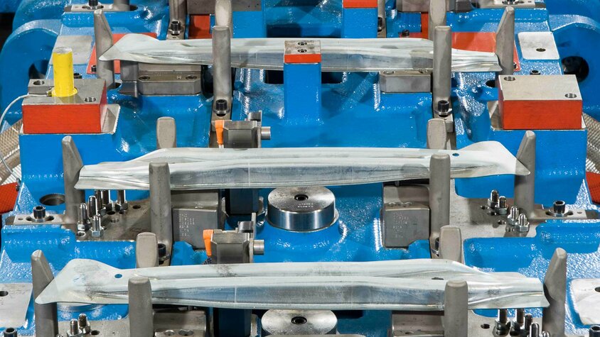 Transferwerkzeug zur Kaltumformung im Detail: Mehrere fixierte Blechteile in einem präzise gefertigten Werkzeug für die Herstellung von Türaufprallträgern in der Automobilindustrie.