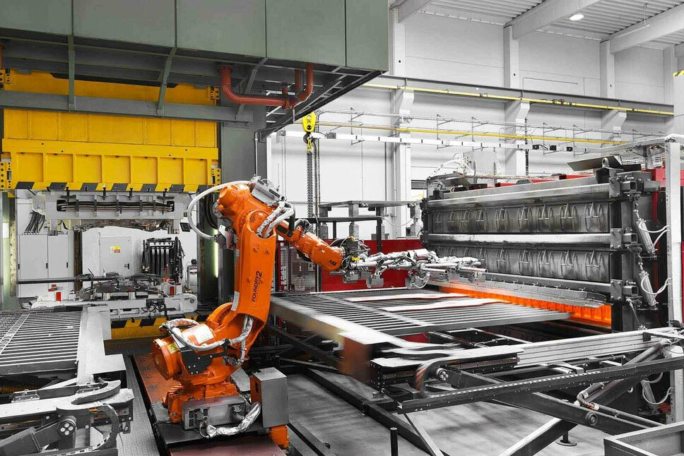 weba Serienfertigung Warmumformanlage Eine Roboterarm entimmt zwei glĂĽhende Formplatinen aus einem Kammerofen, um sie in das Warmumformwerkzeug in der Umformpresse fĂĽr die Serienfertigung zu transferieren