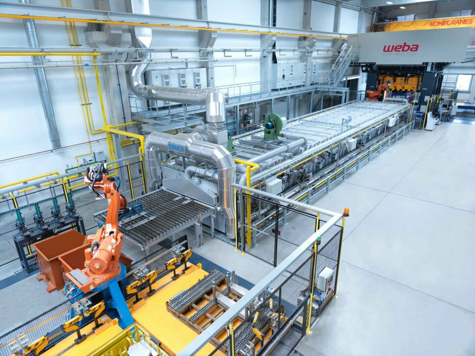 Das Bild zeigt eine Gesamtaufnahme der Presshärtelinie von weba Olomouc. Alle Prozessschritte im Presshärten sind deutlich zu erkennen: von der Markierstation über den Transfer zum Ofen, den Transfer vom Ofen in die Presse bis hin zur Umformpresse.