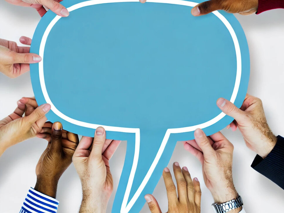Jobs in Steyr - Karriereratgeber Eine Gruppe von verschiedenen Händen, die gemeinsam eine große blaue Sprechblase halten. Die Sprechblase ist leer und symbolisiert Kommunikation und Zusammenarbeit. Der Hintergrund ist schlicht, was die gemeinschaftliche Anstrengung zur Unterstützung der Sprechblase hervorhebt.