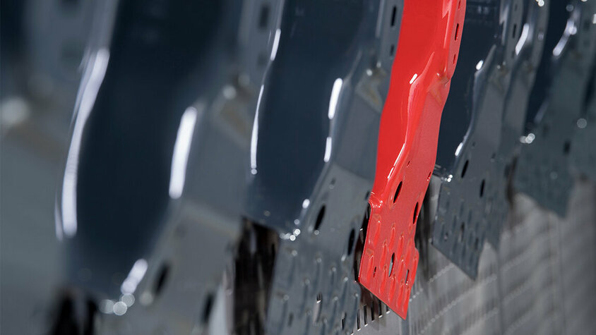 Nahaufnahme einer Reihe von nebeneinander aufgehängten B-Säulen, wobei eine auffällig in Rot und die übrigen in elegantem Anthrazitgrau lackiert sind, was auf die Einzigartigkeit der weba Produkte deutet. 