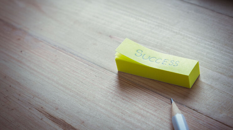 Yellow sticky note with the word "Success" on a wooden table, next to a pencil.