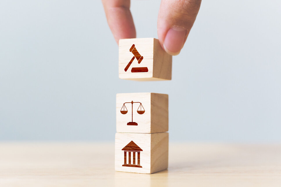 Business Ethics and Compliance with Laws Three wooden blocks in cube form with painted icons representing the theme of justice, symbolizing stability and the rule of law. In the business ethics of weba Werkzeugbau, this image symbolizes the policy for compliance with laws and contracts.