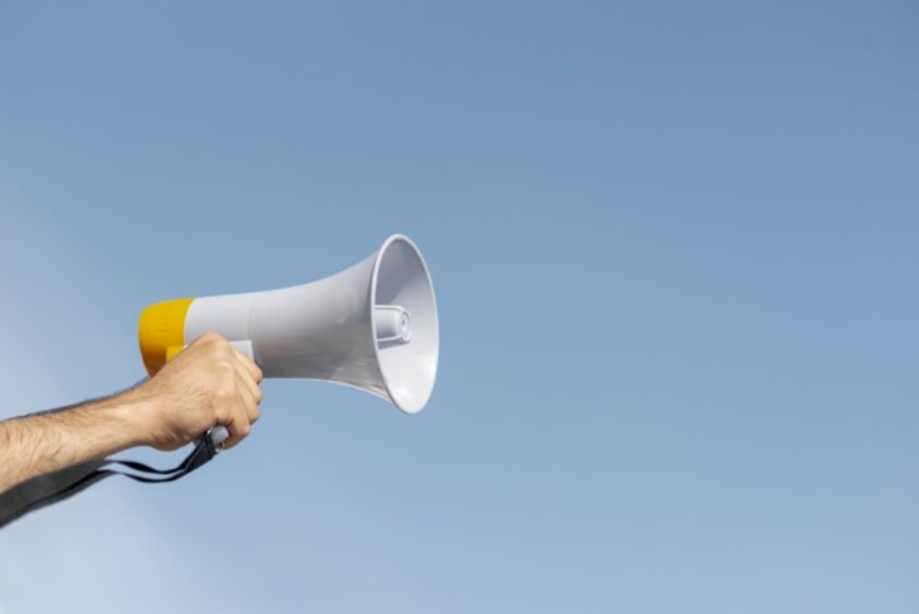 Career Guide A hand holds a megaphone in the air against a blue, cloudless sky, symbolizing a guidebook for job advertisements.