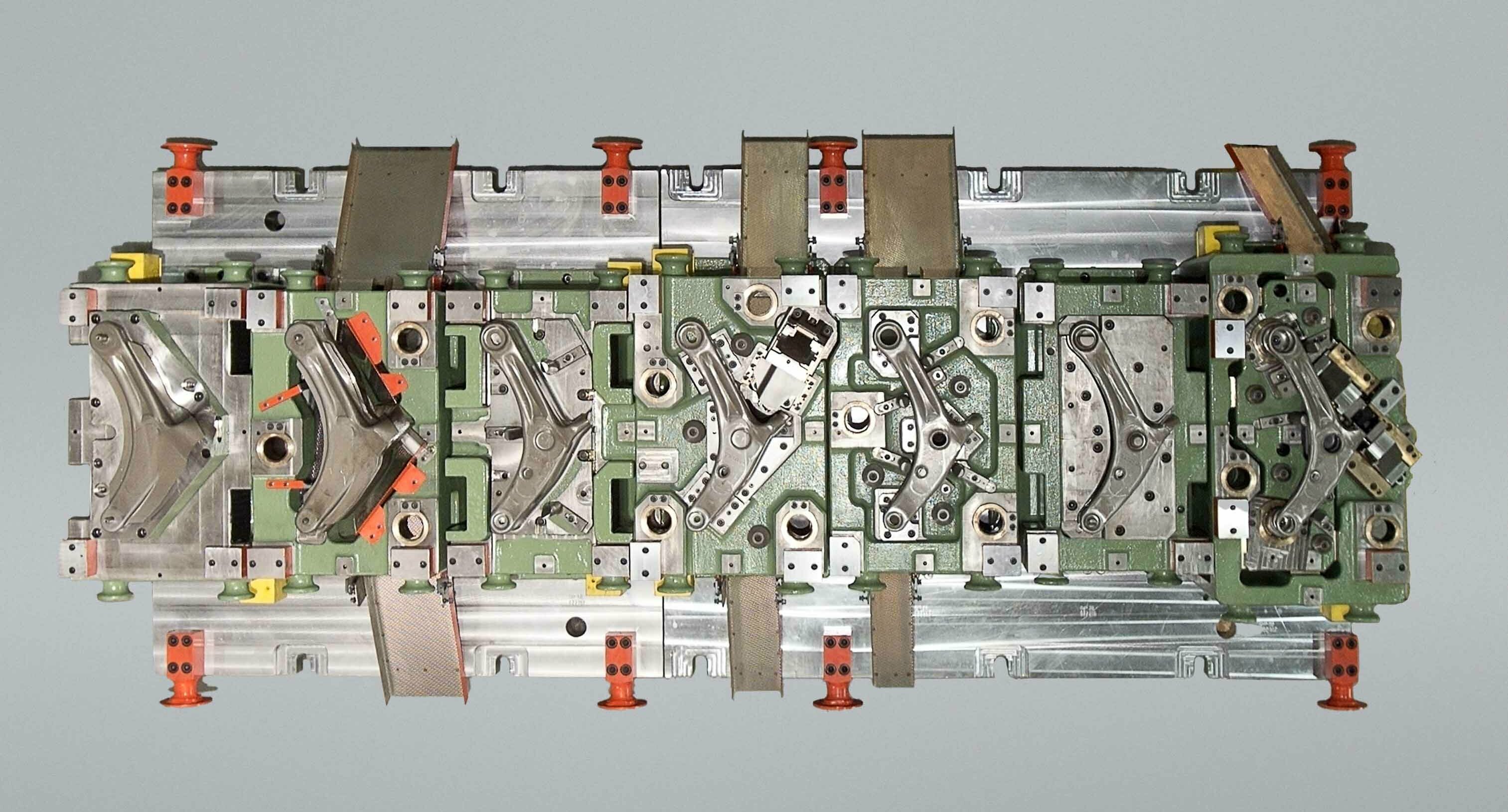 Top view of a transfer tool for manufacturing a control arm; several stations for forming and positioning the part are visible in a multi-stage tool setup.