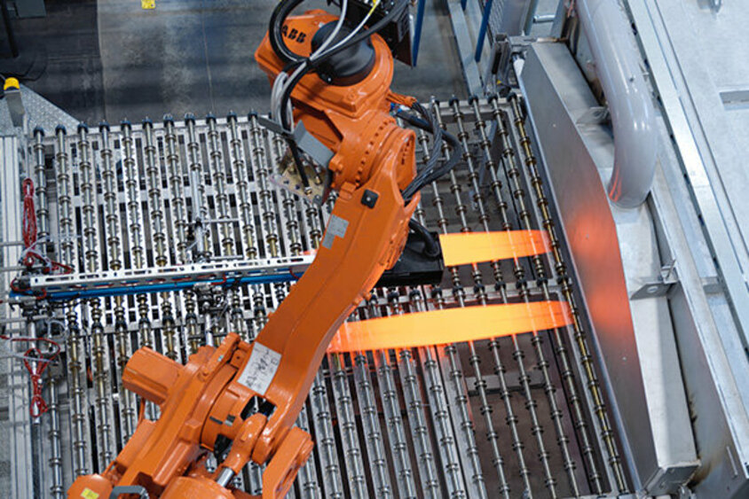 weba Werkzeugbau - Technology Blog about Hot Forming and Tool Manufacturing A robotic arm extracts two glowing blank plates from a continuous furnace, preparing to transfer them into a hot forming tool for shaping.