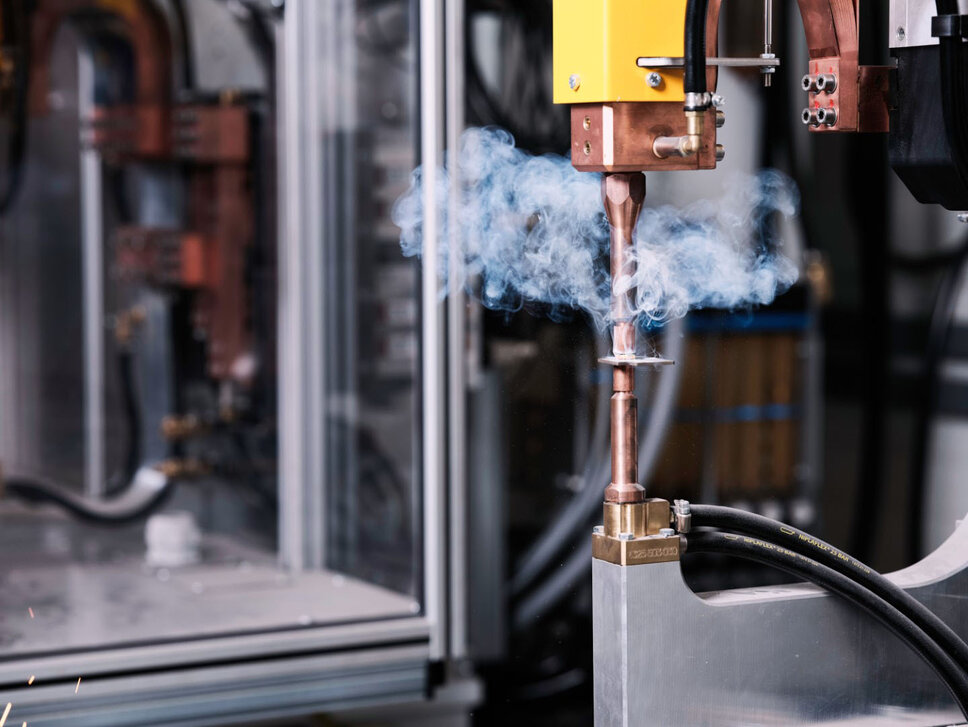 Präzises Punktschweißen im High-Tech-Schweißlabor Nahaufnahme einer industriellen Schweißanlage in einem Schweißlabor. Die Maschine führt präzises Punktschweißen durch, während Rauch aufsteigt. Im Hintergrund sind komplexe technische Geräte und Laboreinrichtungen zu sehen, die für fortschrittliche Schweißprozesse verwendet werden.
