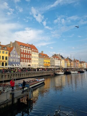 Nyhavn in Copenhagen with colorful houses, boats on the water, and many people along the promenade under a blue sky.