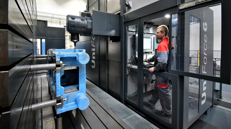 Zerspanungstechnik Jobs in Steyr - weba Werkzeugbau Ein Maschinenbediener steht im Bedienraum eines Bearbeitungszentrums der Marke SHW und beobachtet die Bearbeitung eines großen Gusses.