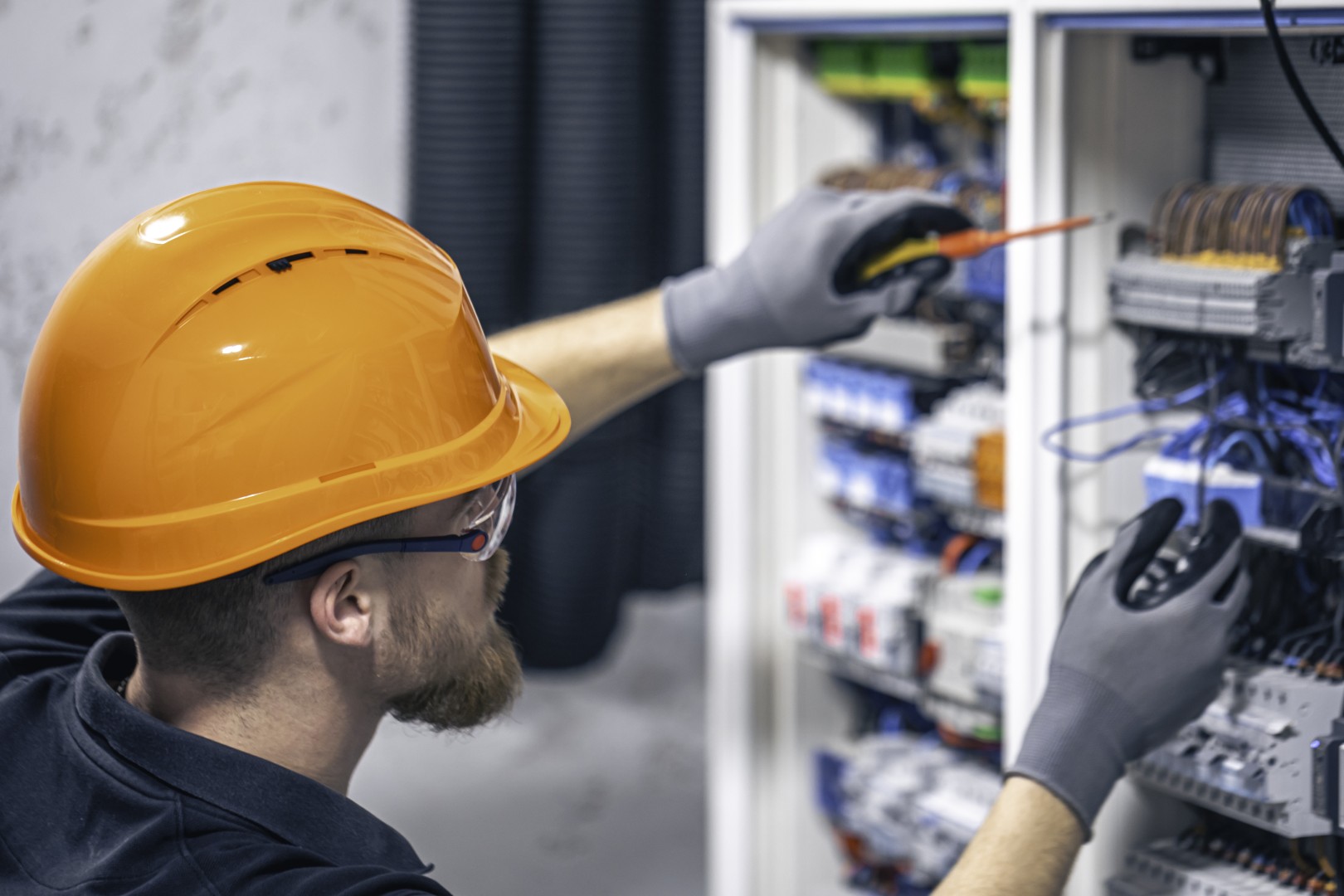 Elektromechaniker mit Schutzhelm prüft elektrische Steuerung und Verkabelung in einem Schaltschrank