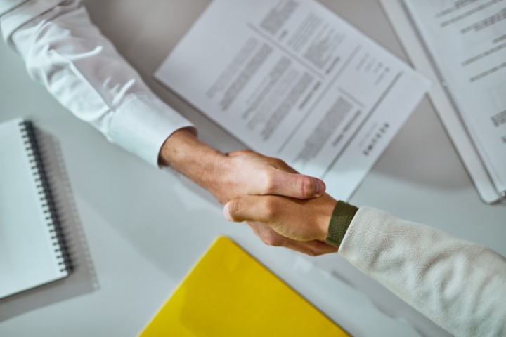 Shaking hands after a successful agreement over signed contracts. The image symbolizes the signing of a contract for a career change.