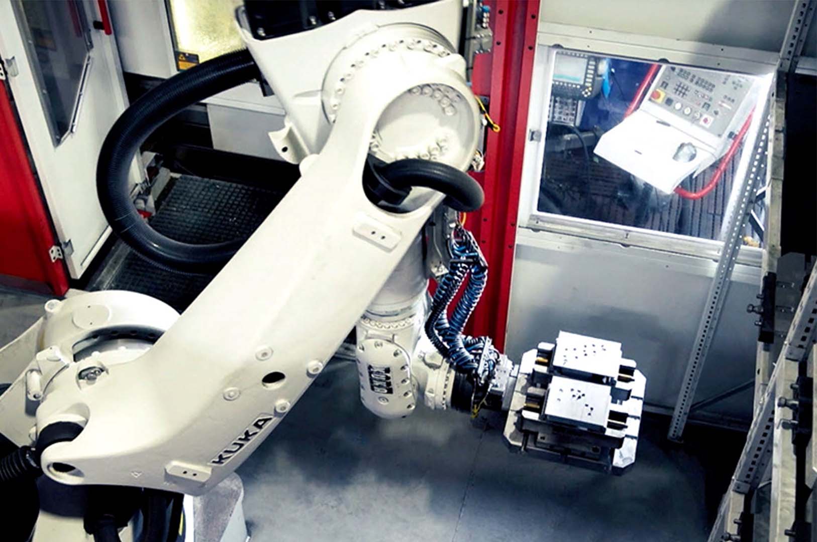 Ein Roboterarm eines automatisierten 5-Achs Bearbeitungszentrums für Einzelteilfertigung entnimmt Stahlblöcke aus dem Palettenwechsler.