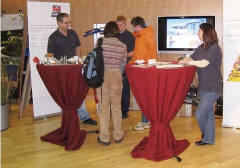 Personen stehen an einem Messestand von weba Werkzeugbau bei der Lehrlingsmesse 2008 in Steyr. Zwei Stehtische mit roten Hussen, Infomaterialien und Werkstücke sind ausgestellt, Besucher informieren sich bei den Mitarbeitern.