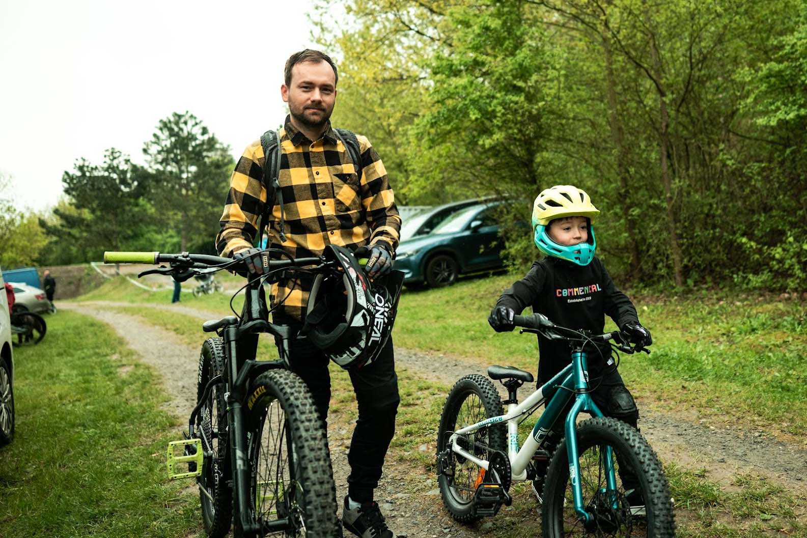 Radek Šimek stands with his mountain bike and helmet next to his young son, who is ready with a kids’ MTB and helmet.