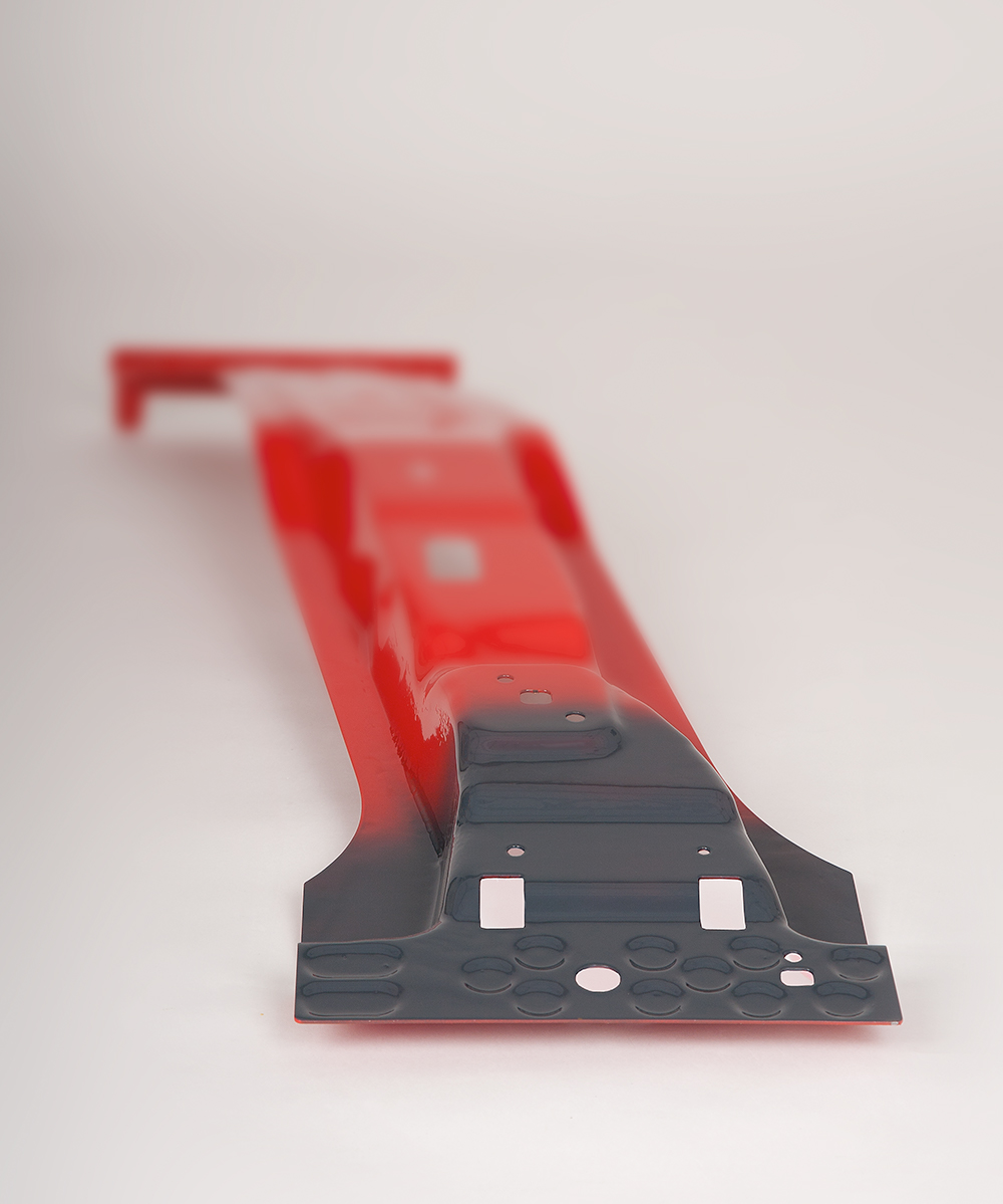 A B-pillar, manufactured from ultra-high-strength material, is shown in a striking red. A SoftZone, specifically developed for customized crash performance, is prominently highlighted in a deep anthracite grey, clearly standing out from the rest of the pillar. The color contrast emphasizes the unique properties of the B-pillar and the technical innovation behind the development of tailored safety features.